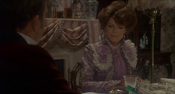 Movie still from “The Seven-Per-Cent Solution” (1976), directed by Herbert Ross – A woman sitting at a dining room table wearing an old fashioned dress; Medium shot, Over the shoulder angle