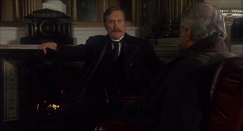 Movie still from “The Seven-Per-Cent Solution” (1976), directed by Herbert Ross – A man in a suit sitting in front of another man in a black suit; Medium shot, Over the shoulder angle