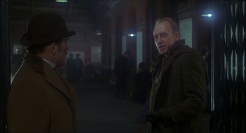 Movie still from “The Seven-Per-Cent Solution” (1976), directed by Herbert Ross – A man in a brown coat and a hat talking to another man in a brown coat and a hat; Medium shot, Over the shoulder angle