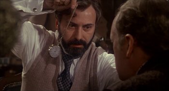 Movie still from “The Seven-Per-Cent Solution” (1976), directed by Herbert Ross – A man with a beard is holding a necklace; Close Up shot, Over the shoulder angle