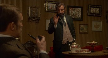 Movie still from “The Seven-Per-Cent Solution” (1976), directed by Herbert Ross – A man in a suit and tie holding up a cell phone; Medium shot, Over the shoulder angle