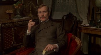 Movie still from “The Seven-Per-Cent Solution” (1976), directed by Herbert Ross – A man sitting in a chair smoking a cigarette and eating a banana; Medium shot, Low angle