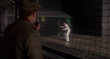Movie still from “The Seven-Per-Cent Solution” (1976), directed by Herbert Ross – A man in a plaid jacket is playing a game of tennis; Wide shot, Over the shoulder angle