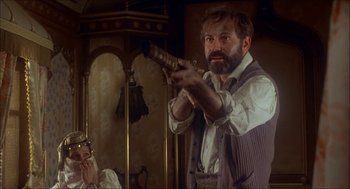 Movie still from “The Seven-Per-Cent Solution” (1976), directed by Herbert Ross – A man with a beard is holding a gun in a room; Medium shot, Low angle