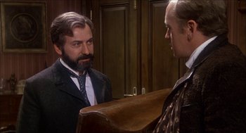 Movie still from “The Seven-Per-Cent Solution” (1976), directed by Herbert Ross – A man in a suit and tie talking to another man in a suit and tie; Medium shot, Over the shoulder angle