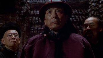 Movie still from “The Shadow” (1994), directed by Russell Mulcahy – An older man wearing a red hat and a purple coat; Close Up shot, Low angle