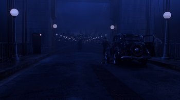 Movie still from “The Shadow” (1994), directed by Russell Mulcahy – A car is parked on the side of the road at night; Extreme Wide shot, High angle