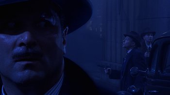 Movie still from “The Shadow” (1994), directed by Russell Mulcahy – A man in a suit and a hat holding a gun; Close Up shot, Over the shoulder angle