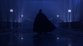 Movie still from “The Shadow” (1994), directed by Russell Mulcahy – A man in a long black coat and a black hat; Wide shot, Low angle