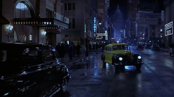 Movie still from “The Shadow” (1994), directed by Russell Mulcahy – A street scene with cars and people on the side of the street; Extreme Wide shot, High angle