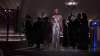 Movie still from “The Shadow” (1994), directed by Russell Mulcahy – A woman in a white dress standing in front of a crowd; Wide shot, Low angle