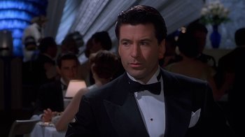 Movie still from “The Shadow” (1994), directed by Russell Mulcahy – A man in a tuxedo standing in front of a group of people; Close Up shot, Over the shoulder angle