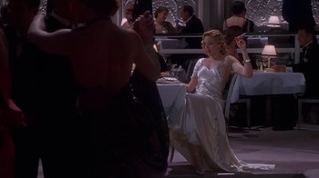 Movie still from “The Shadow” (1994), directed by Russell Mulcahy – A woman in a white dress sitting at a dinner table; Medium shot, Over the shoulder angle