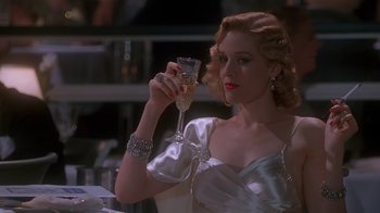 Movie still from “The Shadow” (1994), directed by Russell Mulcahy – A woman holding a glass of wine in her hand; Medium shot, Low angle