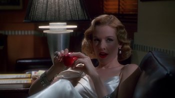Movie still from “The Shadow” (1994), directed by Russell Mulcahy – A woman holding an apple while sitting on a couch; Close Up shot, Low angle