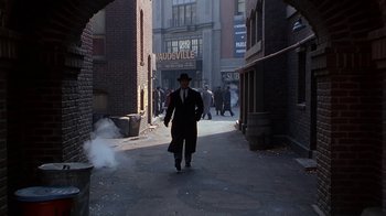 Movie still from “The Shadow” (1994), directed by Russell Mulcahy – A man walking down the street in a suit and hat; Extreme Wide shot, High angle