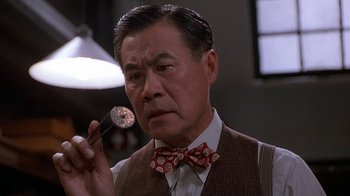 Movie still from “The Shadow” (1994), directed by Russell Mulcahy – An older asian man holding a pipe in his mouth; Close Up shot, Low angle