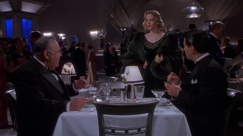 Movie still from “The Shadow” (1994), directed by Russell Mulcahy – Three people sitting at a table in front of a woman in a green dress; Medium shot, Over the shoulder angle