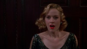 Movie still from “The Shadow” (1994), directed by Russell Mulcahy – A woman with blonde curly hair wearing a black dress; Close Up shot, Over the shoulder angle