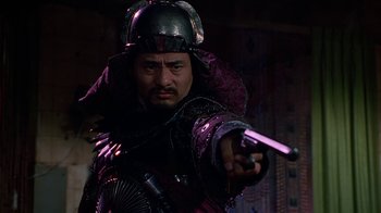 Movie still from “The Shadow” (1994), directed by Russell Mulcahy – A man with a helmet on holding a gun; Close Up shot, Low angle