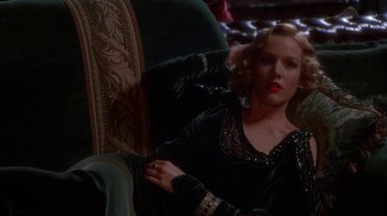 Movie still from “The Shadow” (1994), directed by Russell Mulcahy – A woman sitting in a chair wearing a black dress; Medium shot, High angle