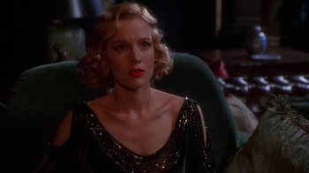 Movie still from “The Shadow” (1994), directed by Russell Mulcahy – A woman with blonde hair sitting in front of a green chair; Close Up shot, Over the shoulder angle