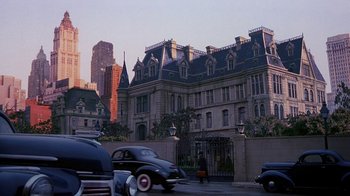 Movie still from “The Shadow” (1994), directed by Russell Mulcahy – An image of cars driving down the street in front of a building; Extreme Wide shot, High angle