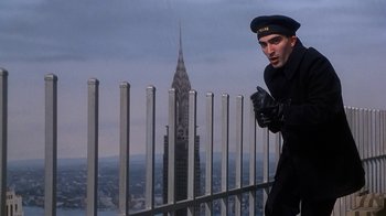 Movie still from “The Shadow” (1994), directed by Russell Mulcahy – A man standing on top of a building near a fence; Medium shot, Low angle
