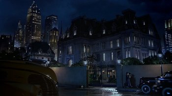 Movie still from “The Shadow” (1994), directed by Russell Mulcahy – Two people standing in front of a building at night; Extreme Wide shot, Low angle
