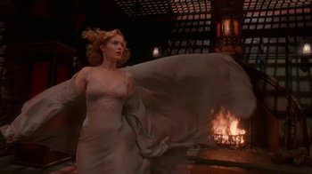 Movie still from “The Shadow” (1994), directed by Russell Mulcahy – A woman standing in front of a fireplace; Wide shot, Low angle