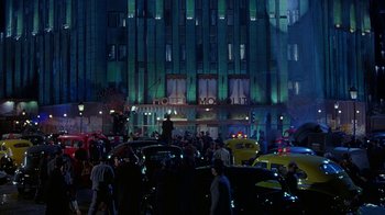 Movie still from “The Shadow” (1994), directed by Russell Mulcahy – A group of people standing around a building at night; Extreme Wide shot, High angle
