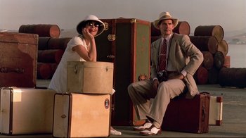 Movie still from “The Sheltering Sky” (1990), directed by Bernardo Bertolucci – A man and a woman sitting next to each other on suitcases; Wide shot, Low angle