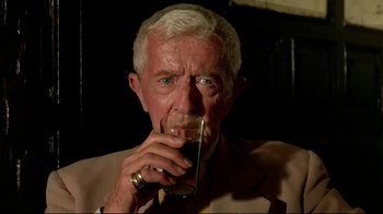 Movie still from “The Sheltering Sky” (1990), directed by Bernardo Bertolucci – An older man drinking a glass of beer; Close Up shot, High angle