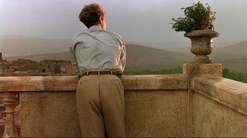 Movie still from “The Sheltering Sky” (1990), directed by Bernardo Bertolucci – A man standing on a ledge looking out at a mountain; Medium shot, Low angle