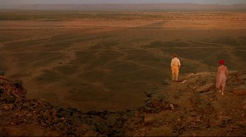 Movie still from “The Sheltering Sky” (1990), directed by Bernardo Bertolucci – A man standing on top of a hill looking out over a desert; Extreme Wide shot, High angle
