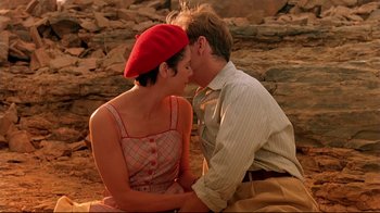 Movie still from “The Sheltering Sky” (1990), directed by Bernardo Bertolucci – A man and a woman sitting next to each other on the ground; Close Up shot, High angle