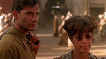 Movie still from “The Sheltering Sky” (1990), directed by Bernardo Bertolucci – A man and a woman standing next to each other on a street; Close Up shot, Over the shoulder angle