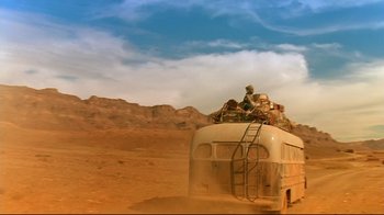 Movie still from “The Sheltering Sky” (1990), directed by Bernardo Bertolucci – An old bus is parked on the side of a dirt road; Extreme Wide shot, Low angle