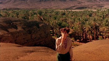 Movie still from “The Sheltering Sky” (1990), directed by Bernardo Bertolucci – A woman standing on top of a hill in front of palm trees; Extreme Wide shot, High angle
