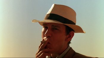 Movie still from “The Sheltering Sky” (1990), directed by Bernardo Bertolucci – A man wearing a hat is smoking a cigarette; Close Up shot, Low angle