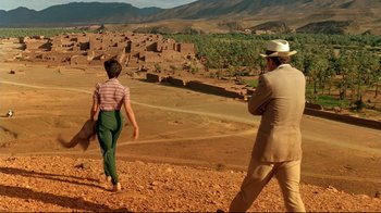 Movie still from “The Sheltering Sky” (1990), directed by Bernardo Bertolucci – A man and a woman walking on a dirt road; Extreme Wide shot, High angle