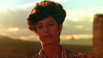 Movie still from “The Sheltering Sky” (1990), directed by Bernardo Bertolucci – A young woman with short brown hair wearing a patterned shirt; Close Up shot, Low angle