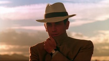 Movie still from “The Sheltering Sky” (1990), directed by Bernardo Bertolucci – A man in a suit and a hat is posing for a picture; Close Up shot, Low angle