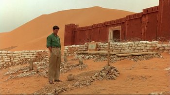 Movie still from “The Sheltering Sky” (1990), directed by Bernardo Bertolucci – A man standing in front of an abandoned building in the middle of the desert; Wide shot, Low angle