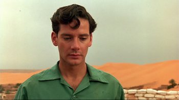 Movie still from “The Sheltering Sky” (1990), directed by Bernardo Bertolucci – A man in a green shirt is standing in front of some sand dunes; Close Up shot, Over the shoulder angle