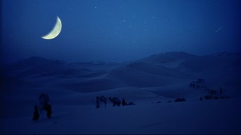 Movie still from “The Sheltering Sky” (1990), directed by Bernardo Bertolucci – A group of people sitting in the snow under a moon; Extreme Wide shot, High angle