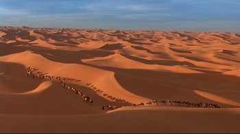 Movie still from “The Sheltering Sky” (1990), directed by Bernardo Bertolucci – A group of people walking across a sandy desert; Extreme Wide shot, High angle