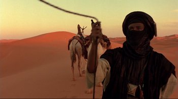 Movie still from “The Sheltering Sky” (1990), directed by Bernardo Bertolucci – A man standing in the desert with two horses; Medium shot, Low angle
