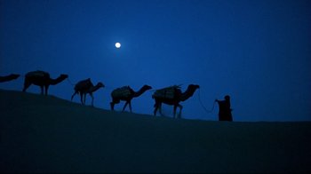 Movie still from “The Sheltering Sky” (1990), directed by Bernardo Bertolucci – A man leading a herd of camels up a hill; Extreme Wide shot, Low angle