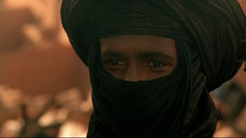 Movie still from “The Sheltering Sky” (1990), directed by Bernardo Bertolucci – A man wearing a black turban and a black head covering; Close Up shot, Over the shoulder angle